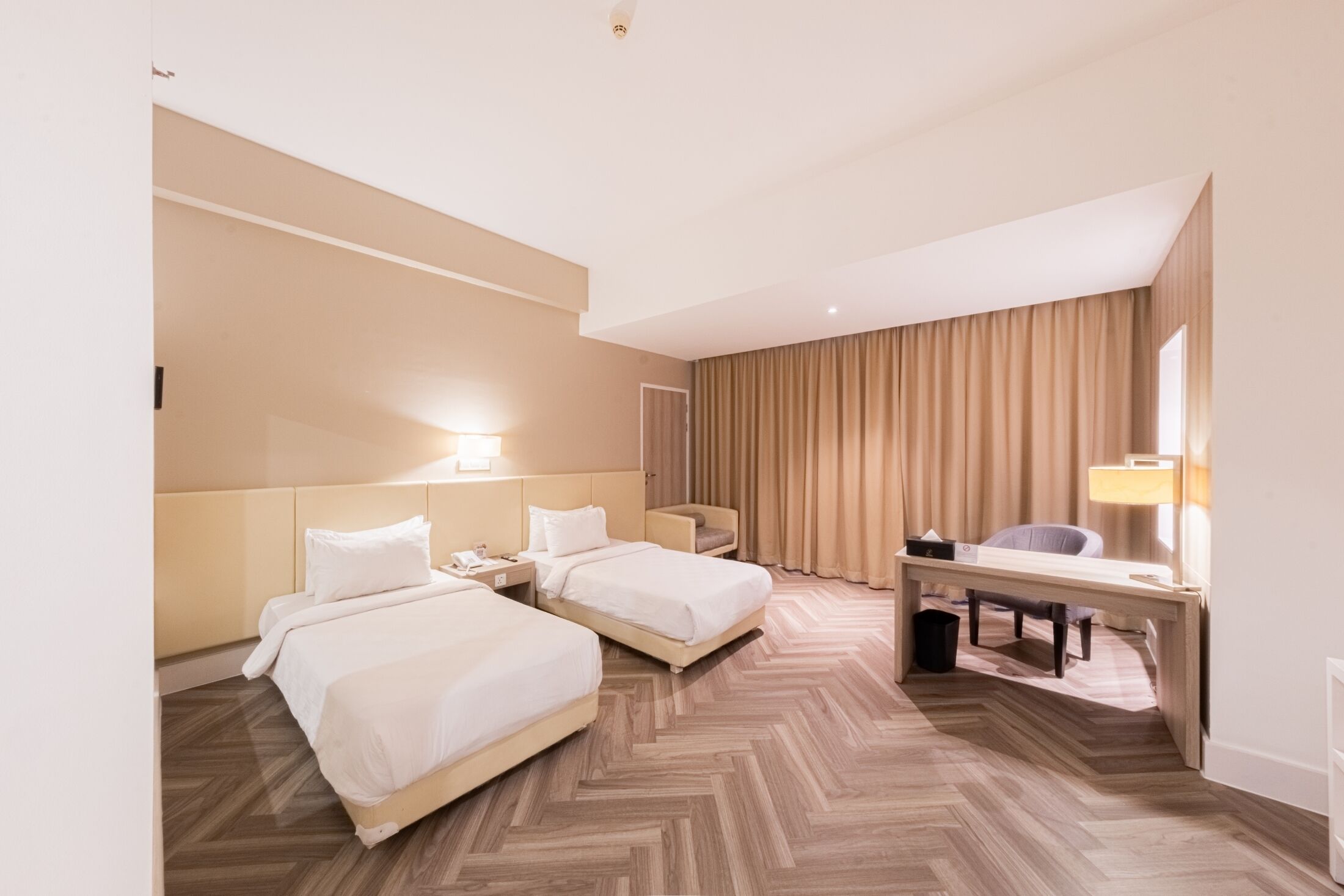 A hotel room with two beds, a desk, a chair, and a large window with curtains.