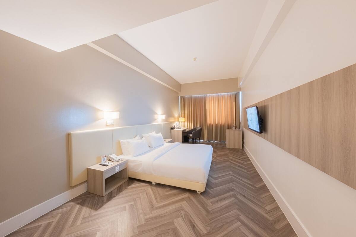 Habitació d'hotel amb un llit gran, taules de nit, escriptori, cadira i televisió penjada a la paret.