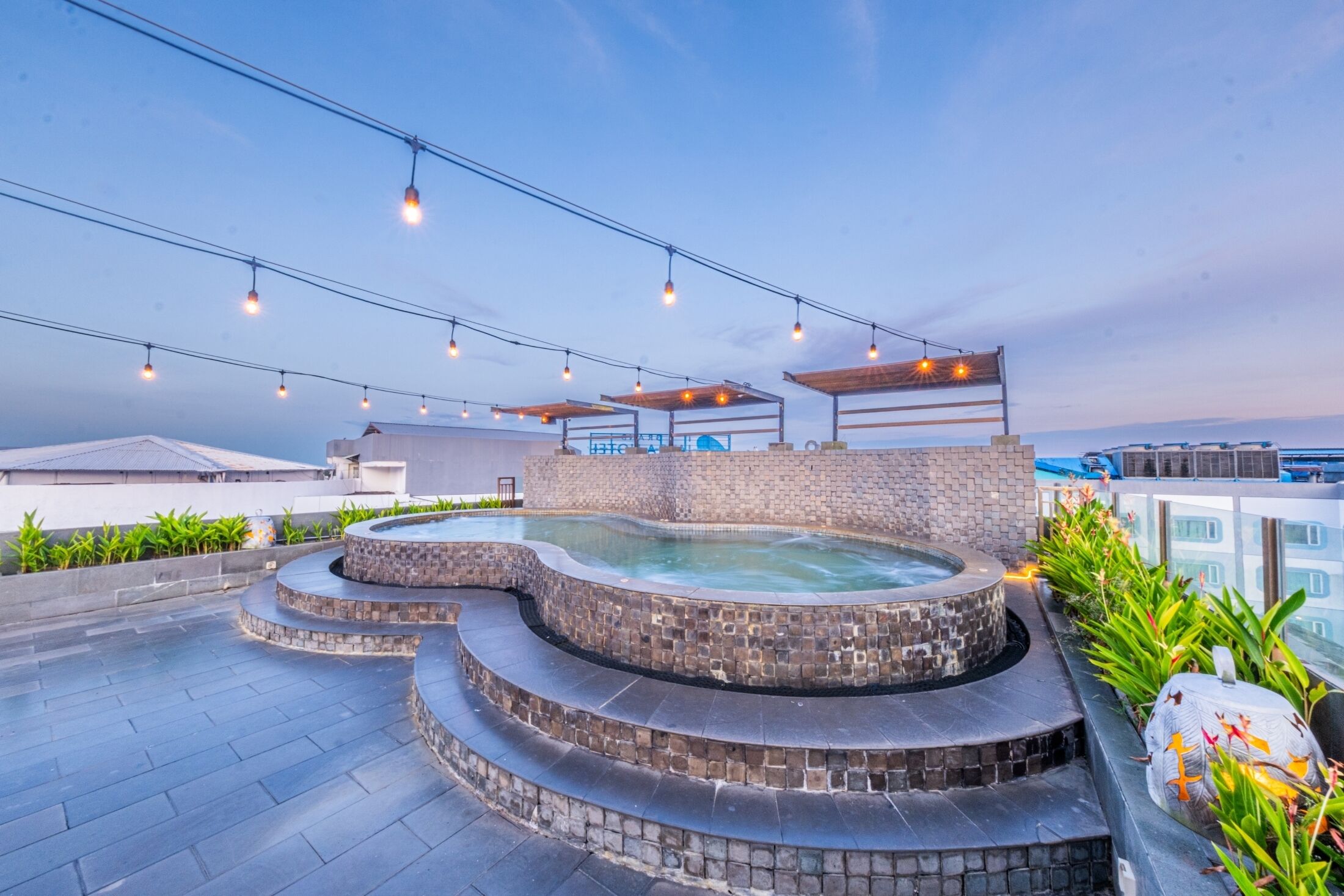 Un área de spa en la azotea con un jacuzzi, mobiliario exterior e iluminación colgante.
