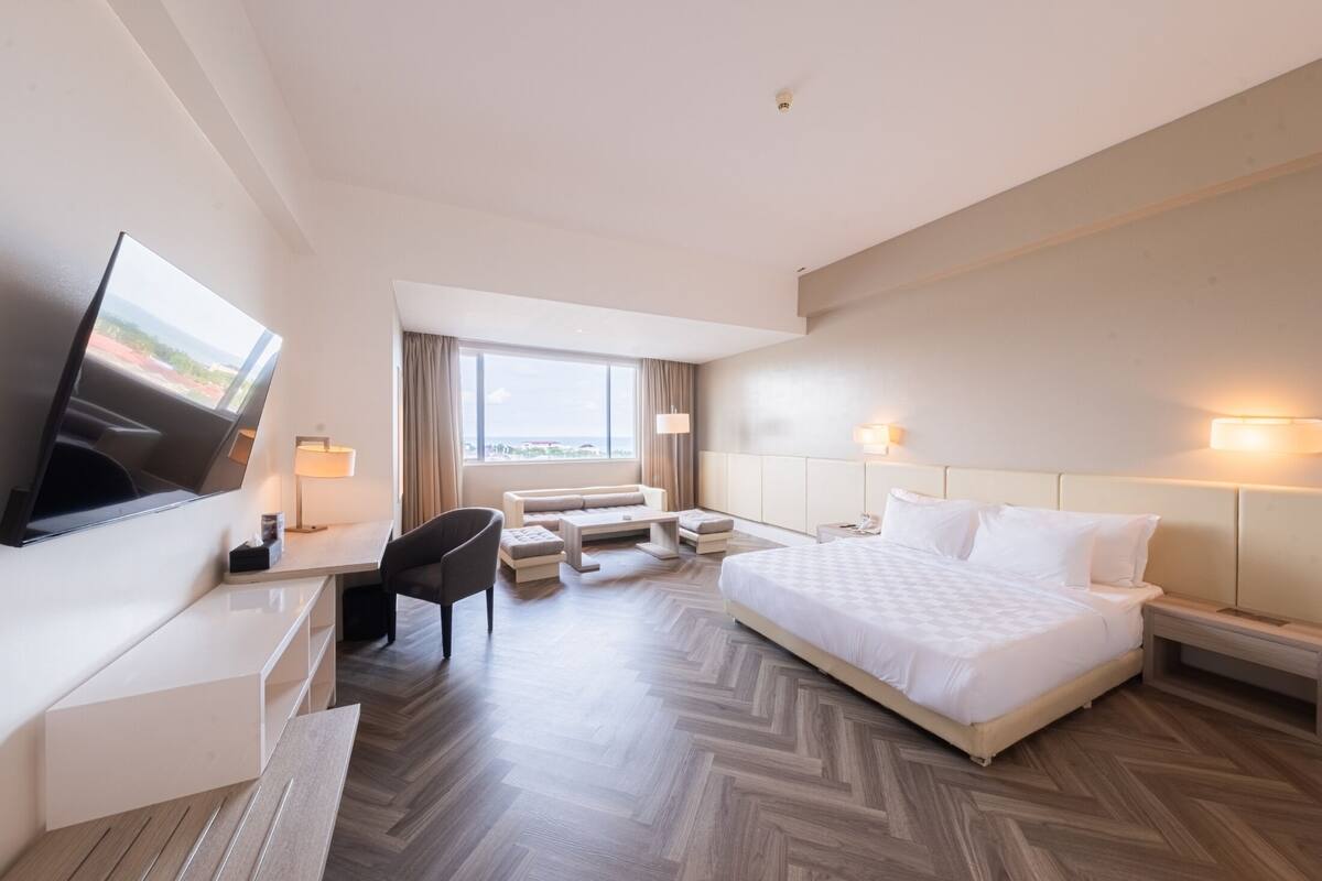 Habitació d'hotel amb llit, escriptori, cadira, televisió i una finestra gran amb vistes.