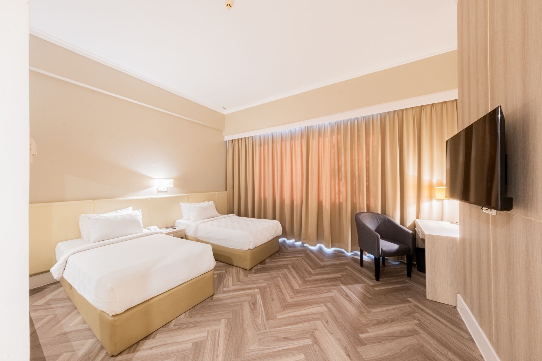 Habitación de hotel con dos camas, un escritorio, una silla, un televisor de pantalla plana y una ventana con cortinas.
