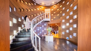 Un hall d’hôtel moderne avec un escalier en colimaçon, un comptoir d’accueil et un vase décoratif posé sur une table.