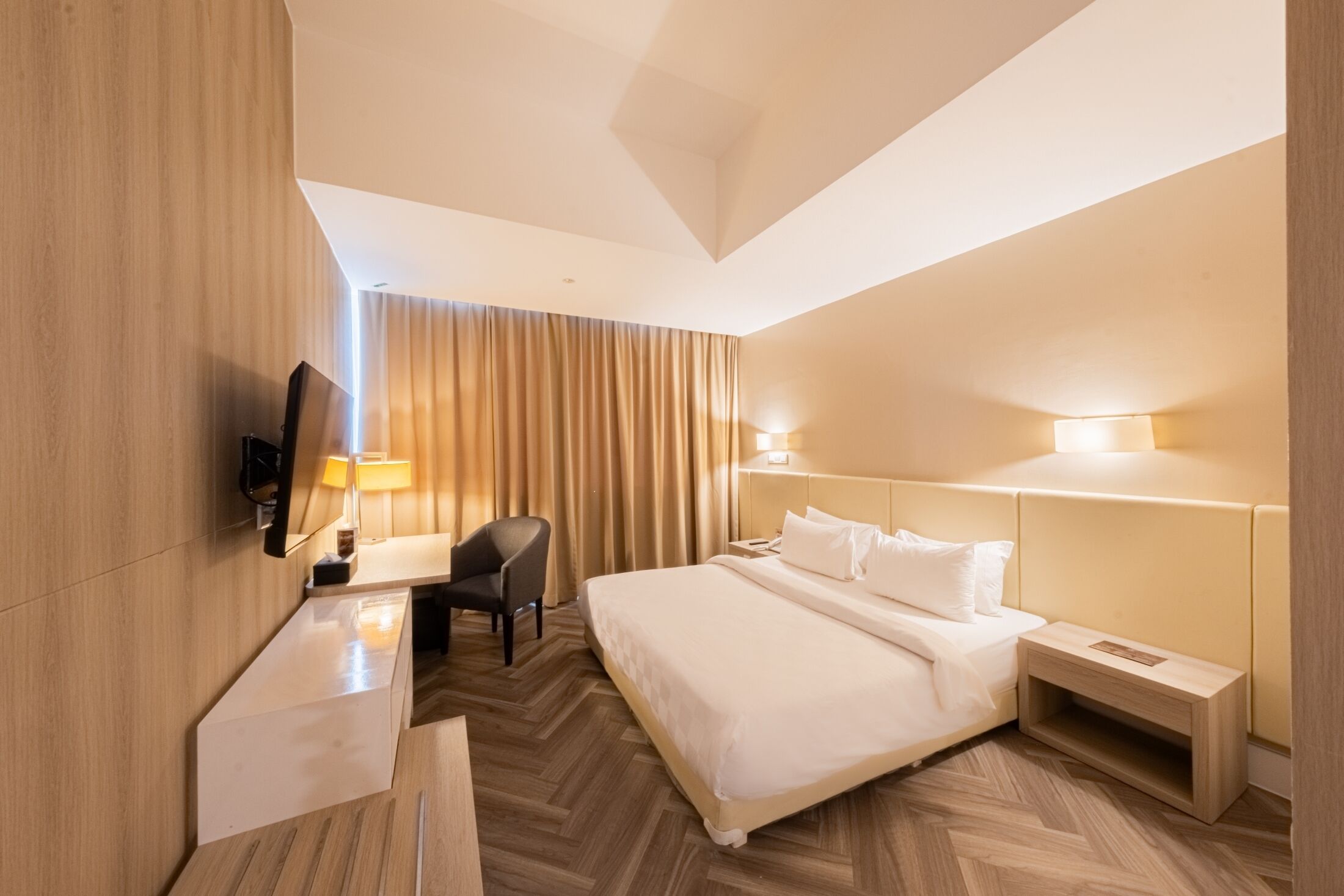 A modern hotel room with a large bed, a desk, a chair, and a TV.