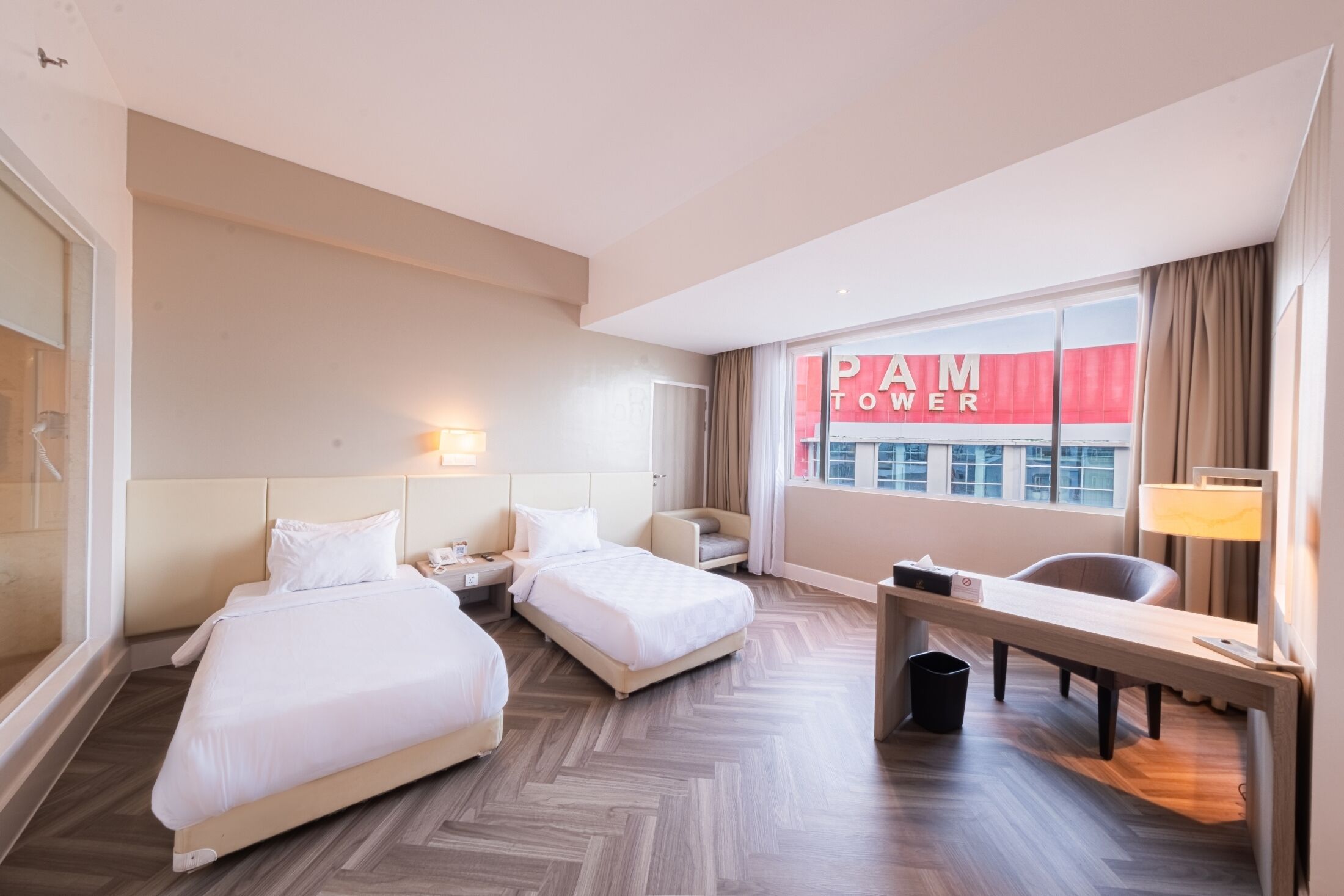 Habitación de hotel con dos camas, un escritorio, una silla, una lámpara y vistas a la ciudad.