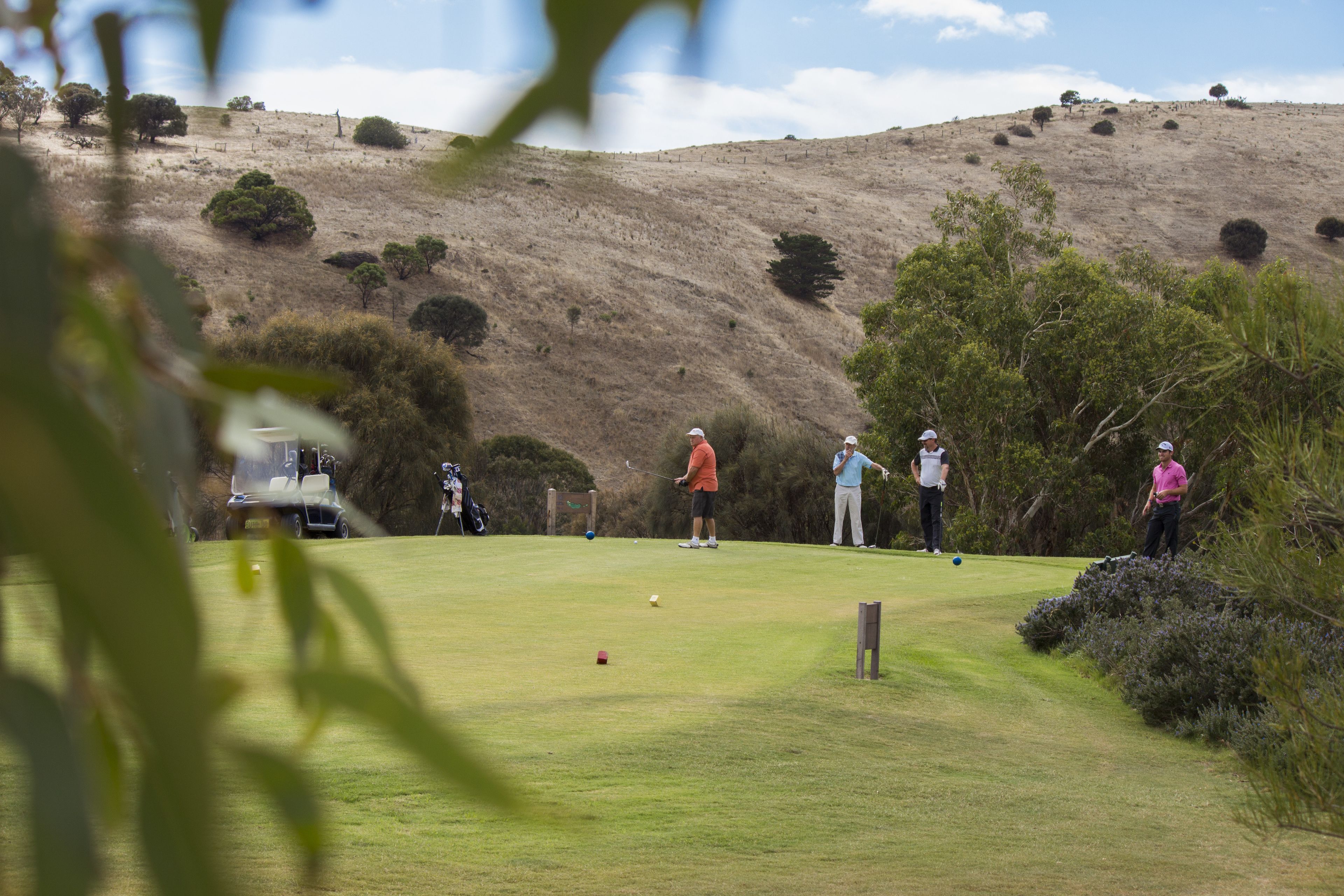 A golf course with players, a clubhouse, and a hilly backdrop.
