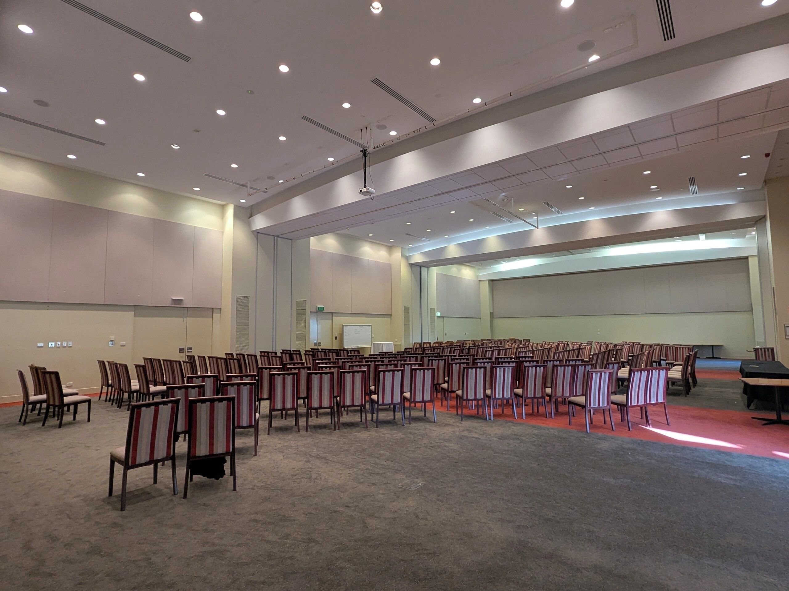 A large conference room with rows of chairs, a stage with a screen, and a carpeted floor.