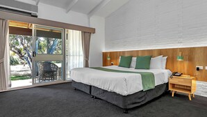 A hotel room with a large bed, a wooden headboard, a nightstand with a lamp, and a view through a glass door. - BreakFree Wirrina Cove (Wirrina Cove)