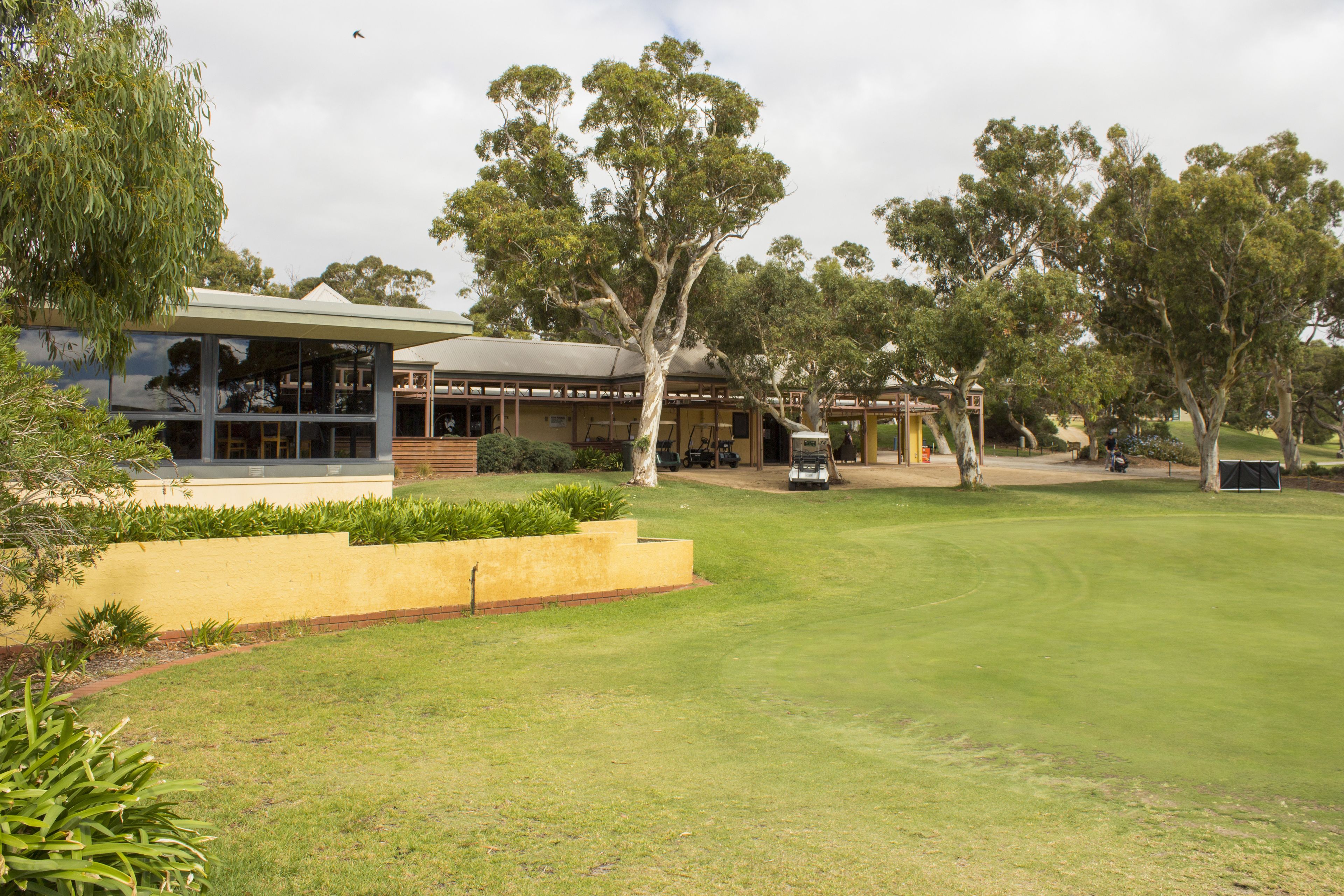 Un campo de golf con un club de campo, una zona de estacionamiento y un árbol grande al frente.
