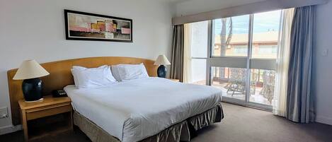 A hotel room with a large bed, two bedside tables with lamps, a framed picture on the wall, and a large window with curtains.