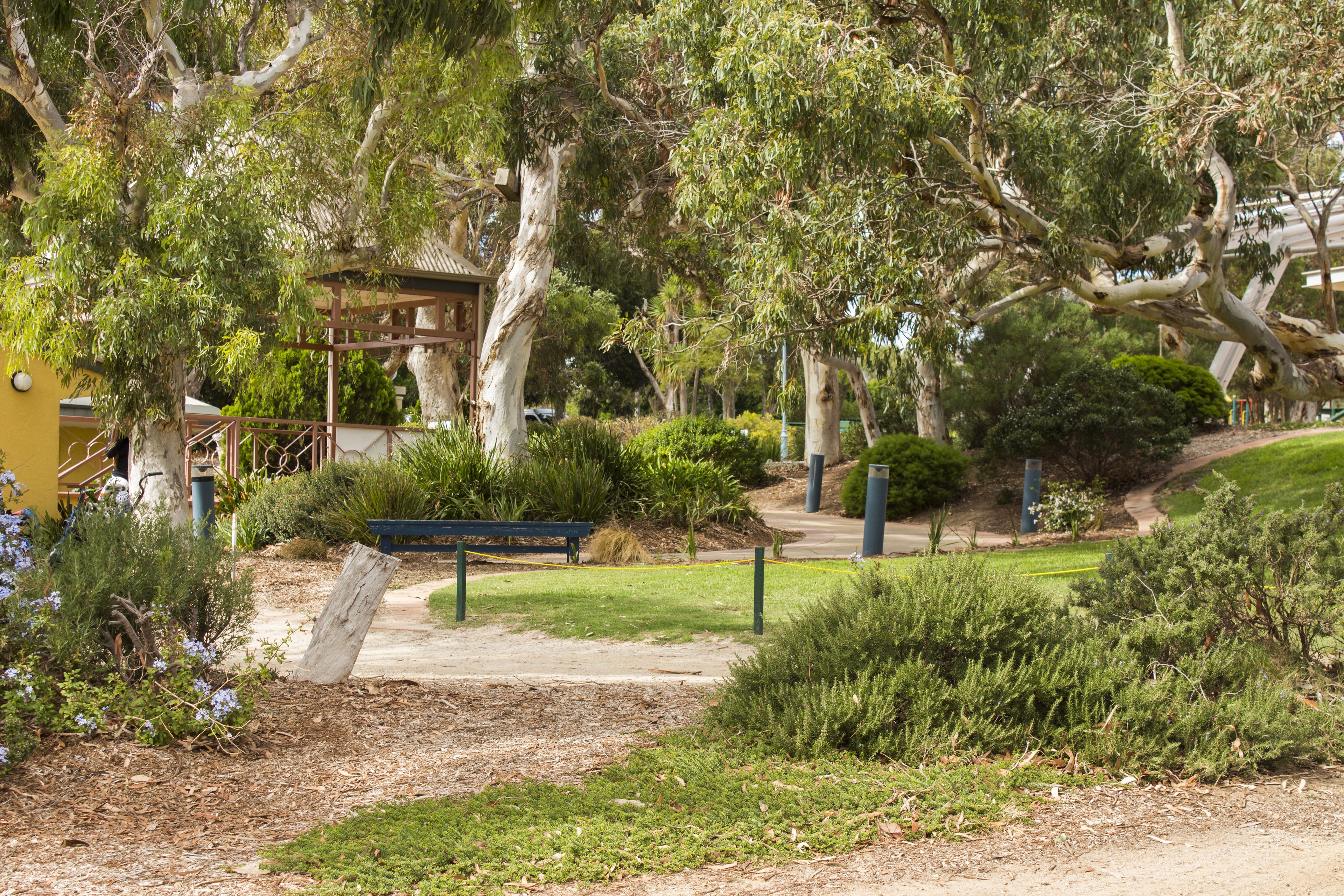 Un parc avec un kiosque en bois, un banc et un sentier.