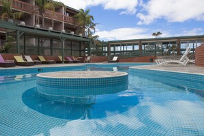 A swimming pool with lounge chairs and a hot tub, surrounded by a building with large windows and a balcony. - BreakFree Wirrina Cove (Wirrina Cove)