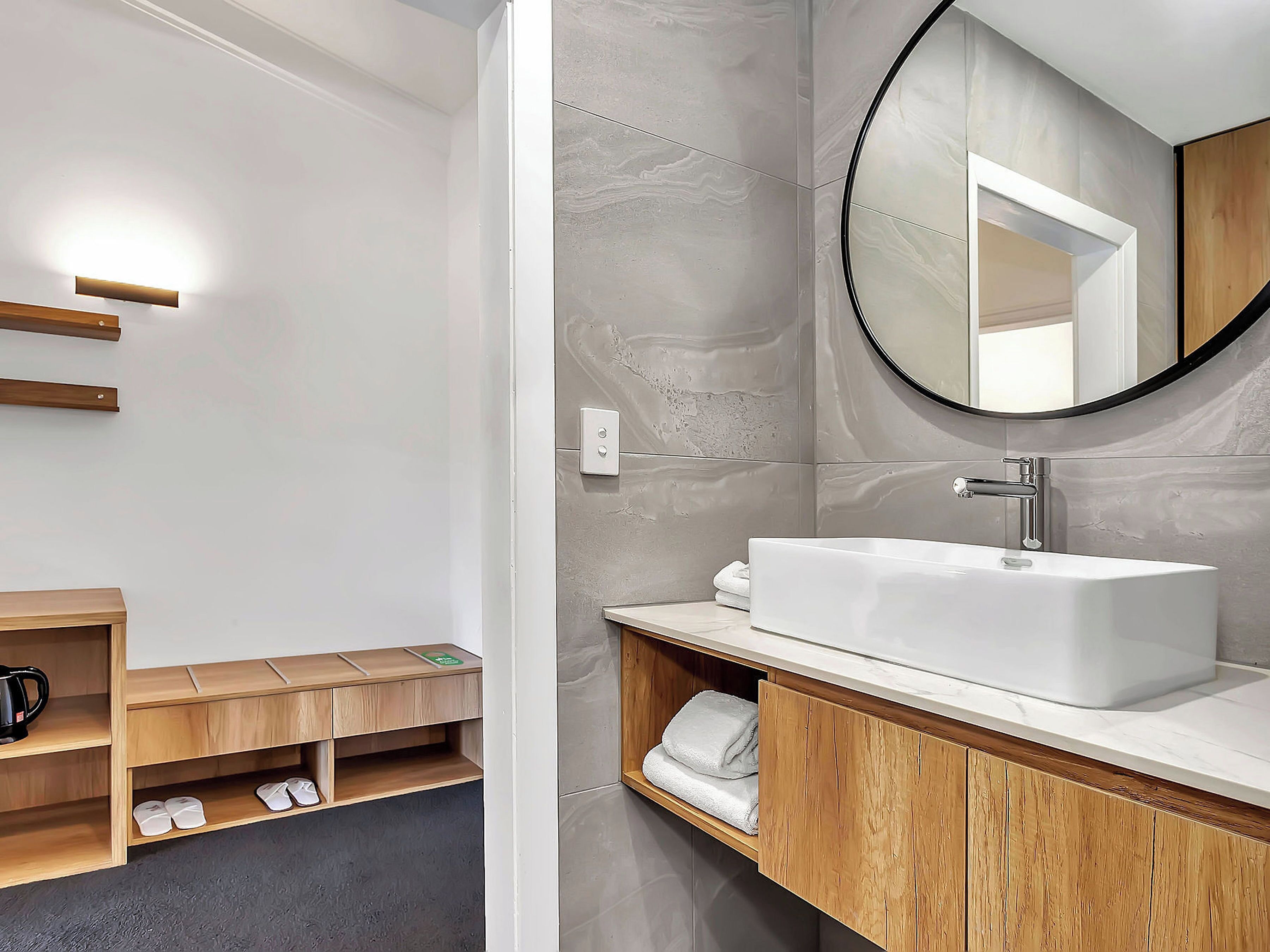 A modern bathroom with a white sink, wooden vanity, and a round mirror.
