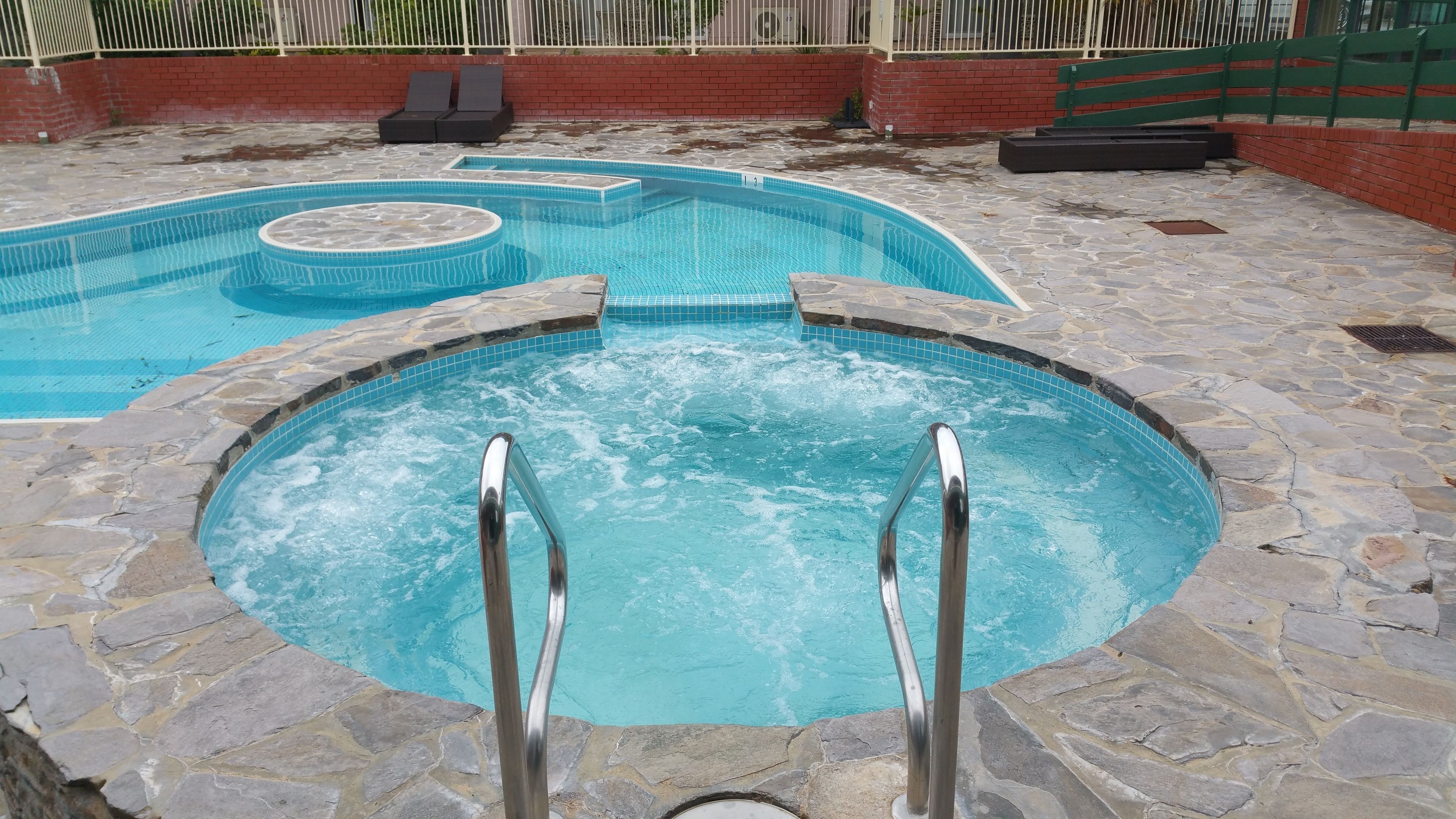 A swimming pool with a stone border and a hot tub in the center.