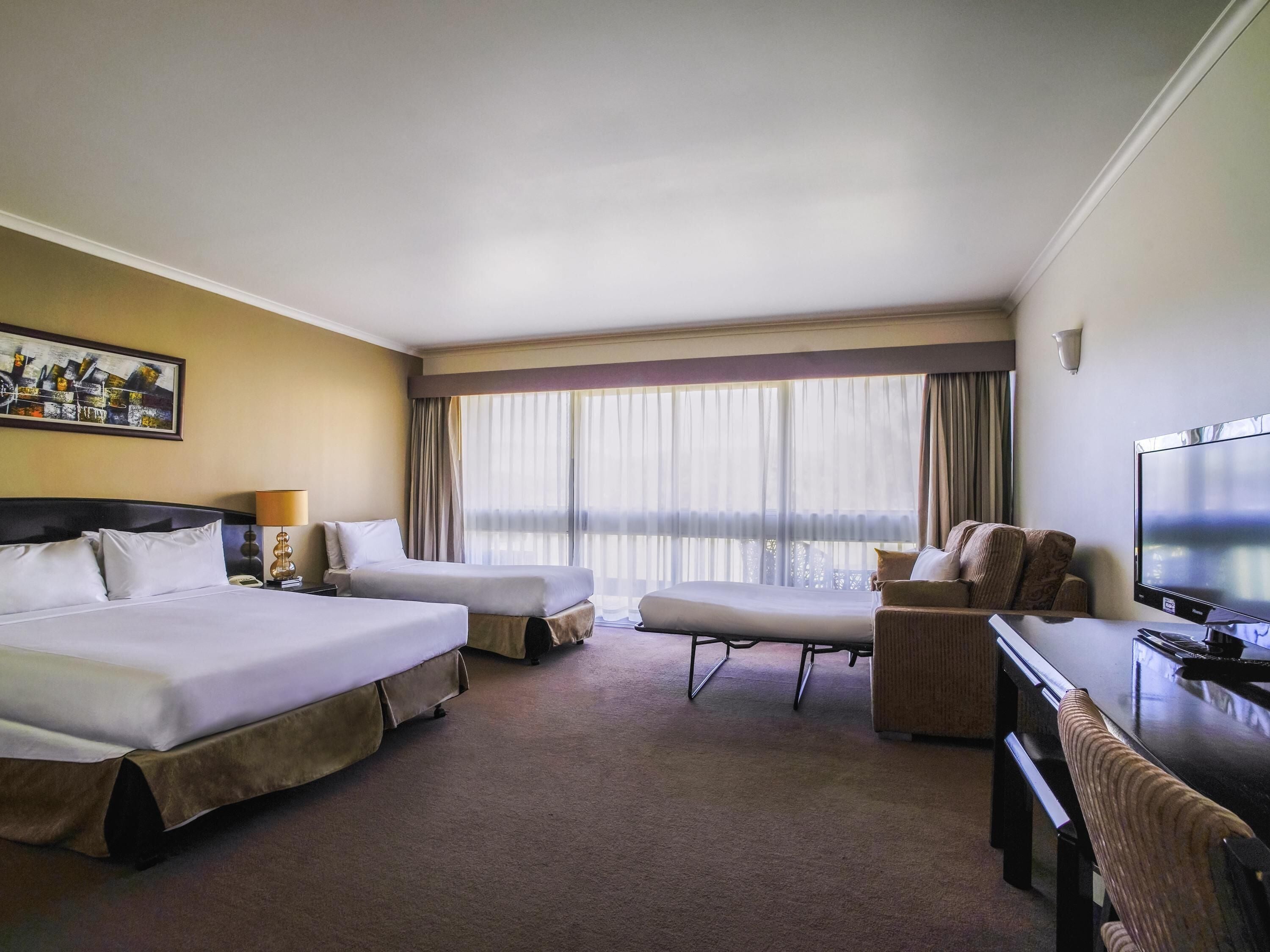 A hotel room with two beds, a desk, a chair, a television, and a large window with curtains.