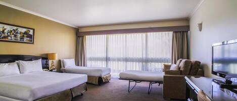 A hotel room with two beds, a desk, a chair, a television, and a large window with curtains.
