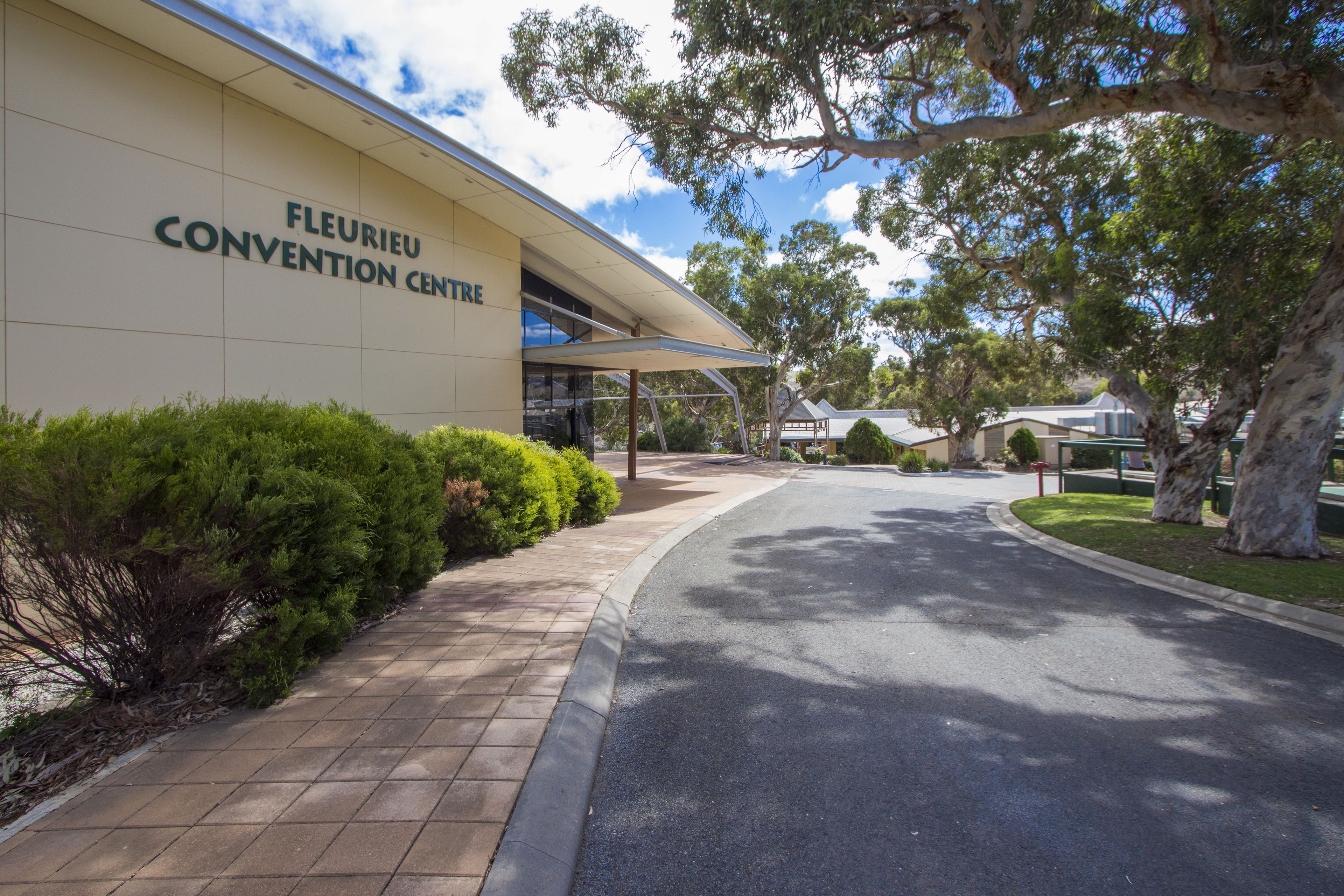The exterior of the Fleurieu Convention Centre with a paved entrance, surrounding greenery, and a clear sky.