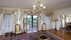 A spacious room with a large window, two upholstered chairs, a patterned rug, and a chandelier. - The Residence at Barossa Chateau (Lyndoch)