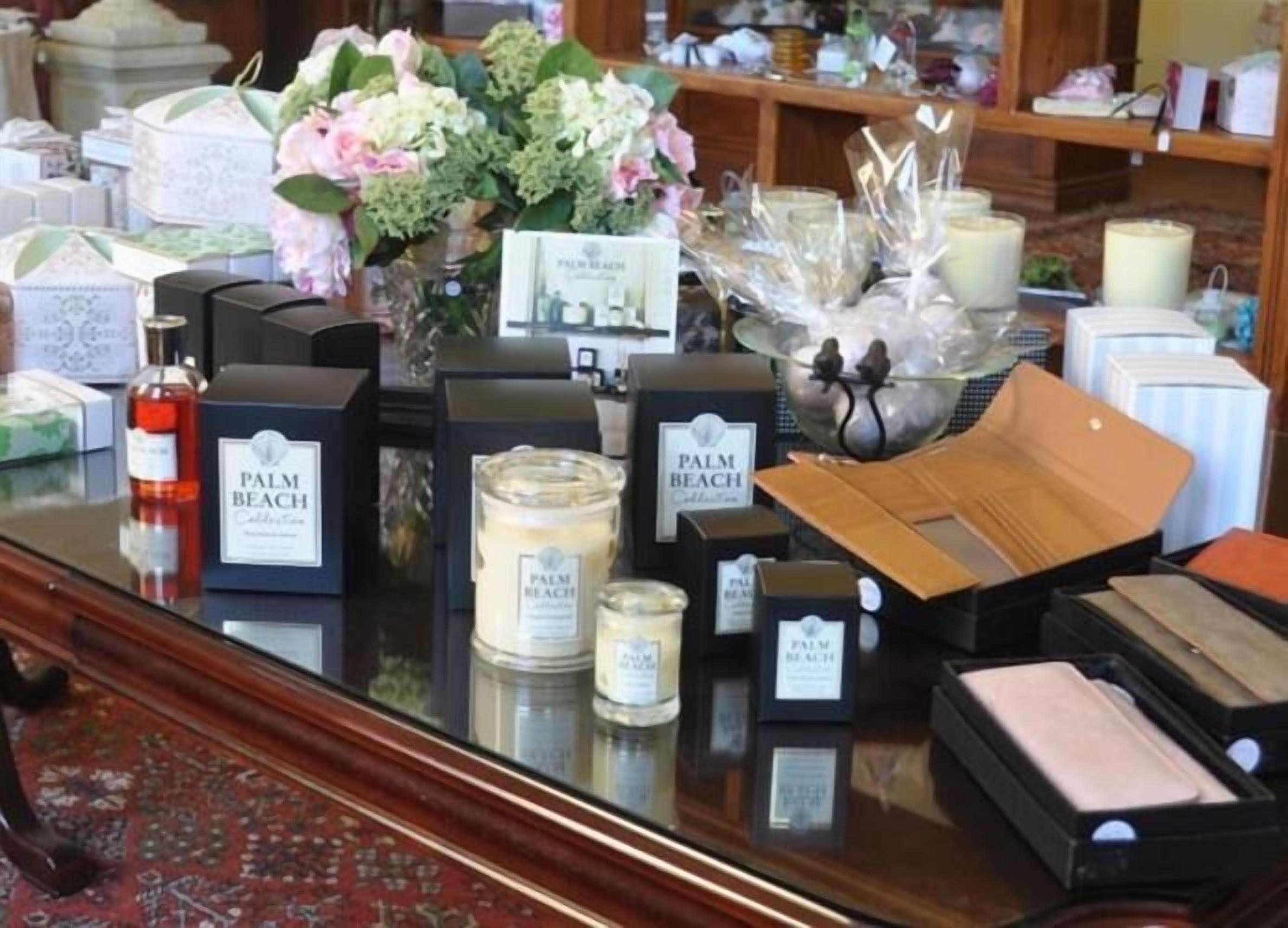A display of Palm Beach Collection products including candles, a bottle, and a vase with flowers.