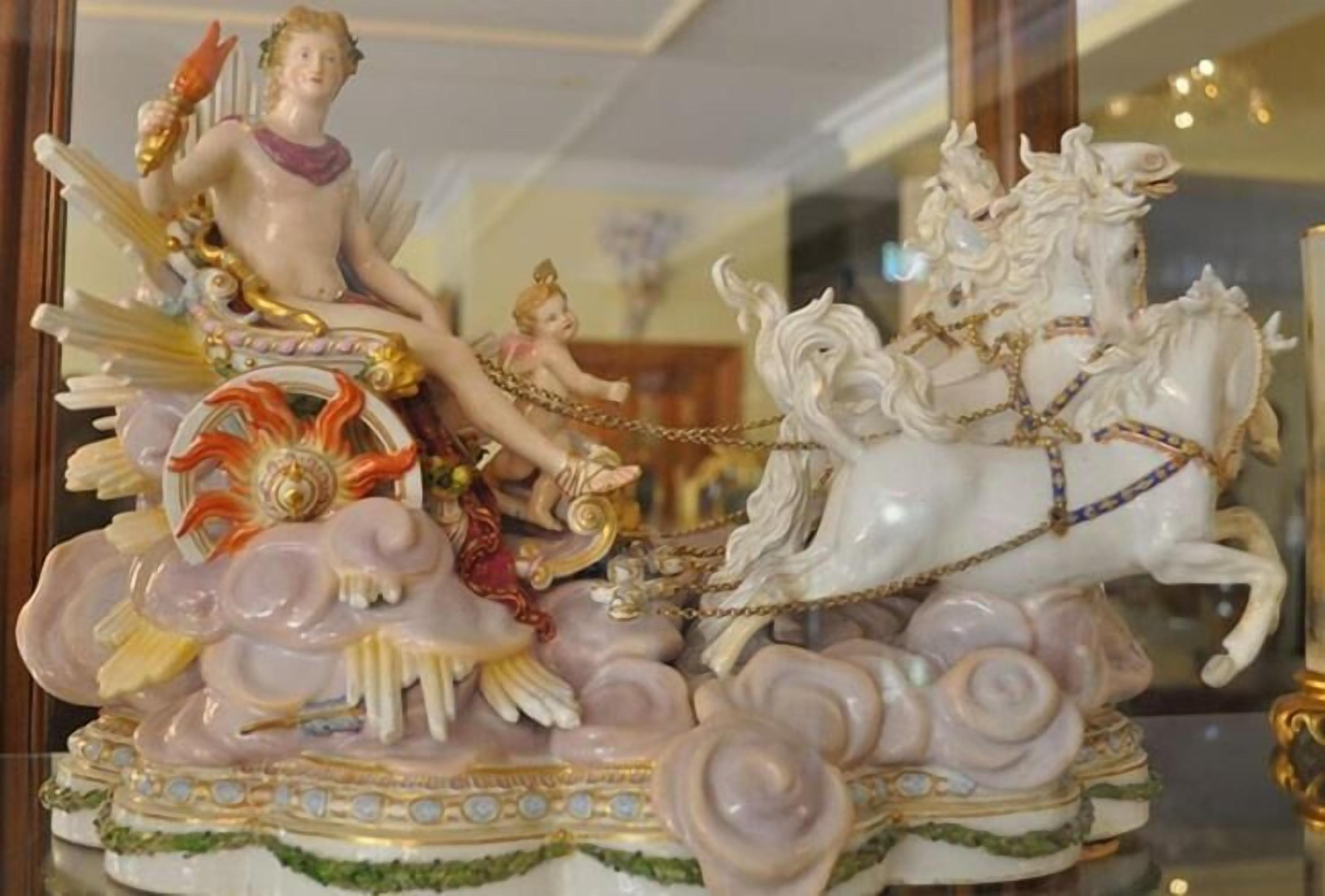 A decorative ceramic sculpture with a figure on a chariot pulled by horses, surrounded by floral patterns.