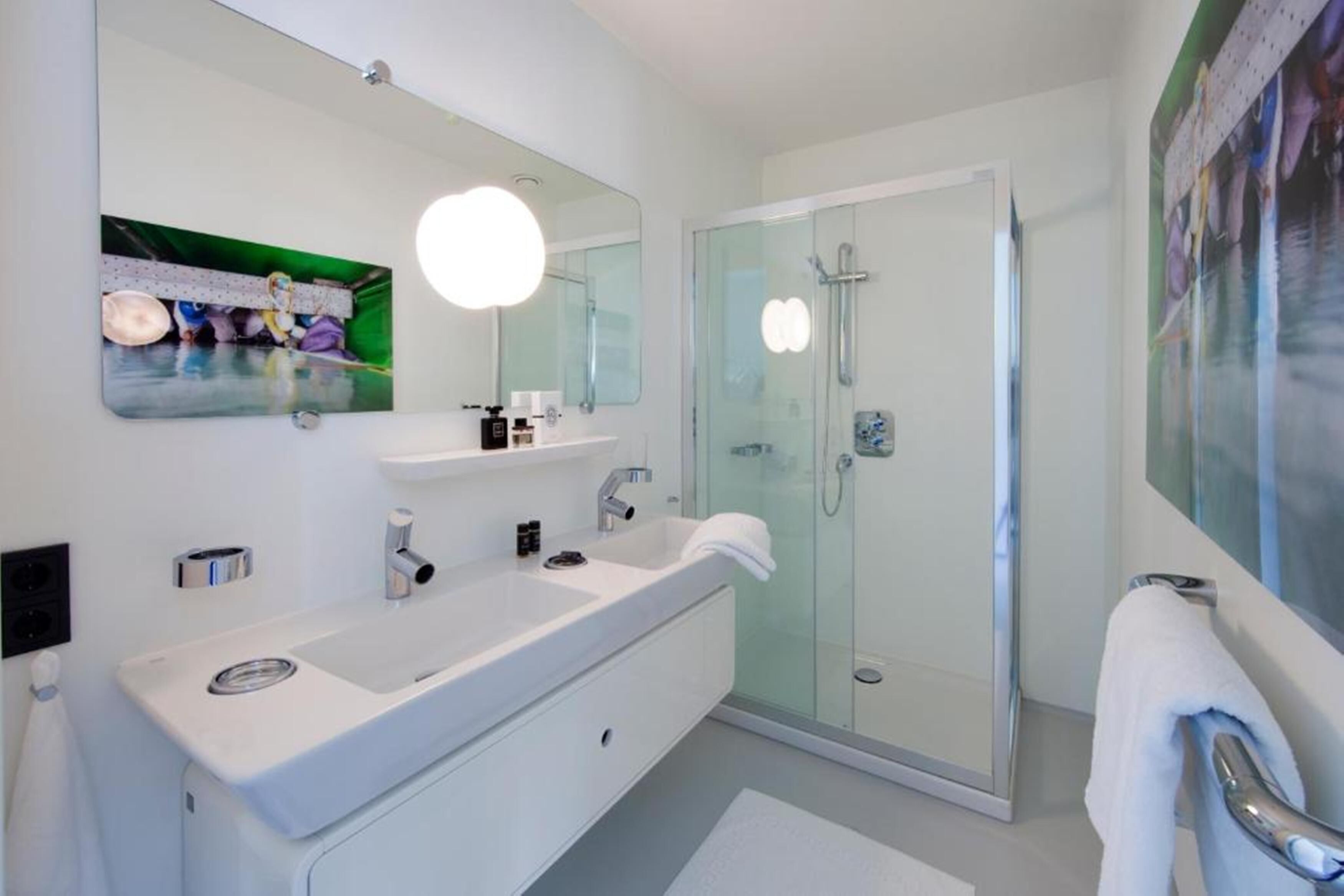 A modern bathroom with a large mirror, a white sink, a glass shower enclosure, and a towel rack.