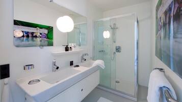 A modern bathroom with a large mirror, a white sink, a glass shower enclosure, and a towel rack.