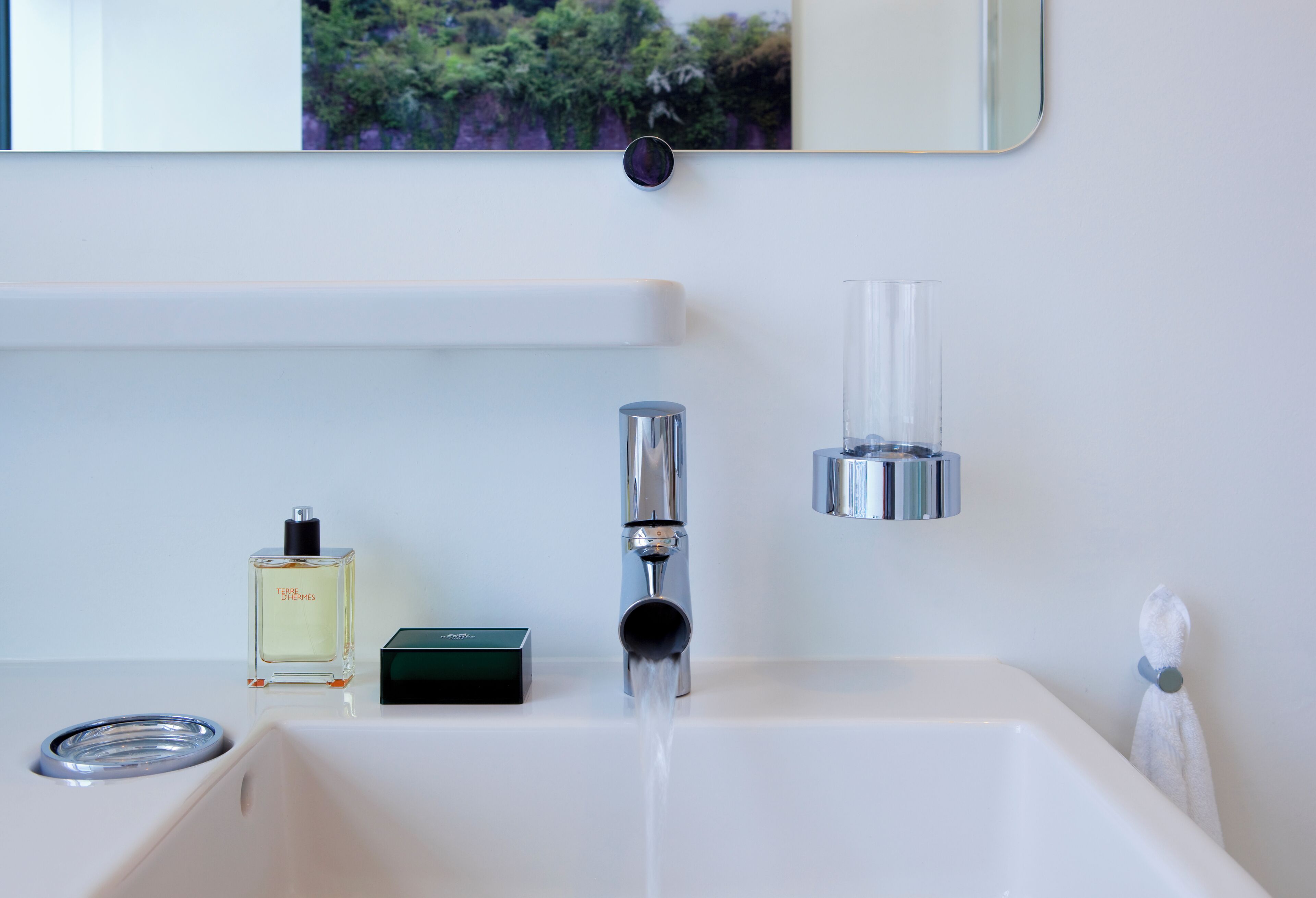 A modern bathroom with a white sink, chrome faucet, and a mirror above. A bottle of perfume and a soap dispenser are on the sink.
