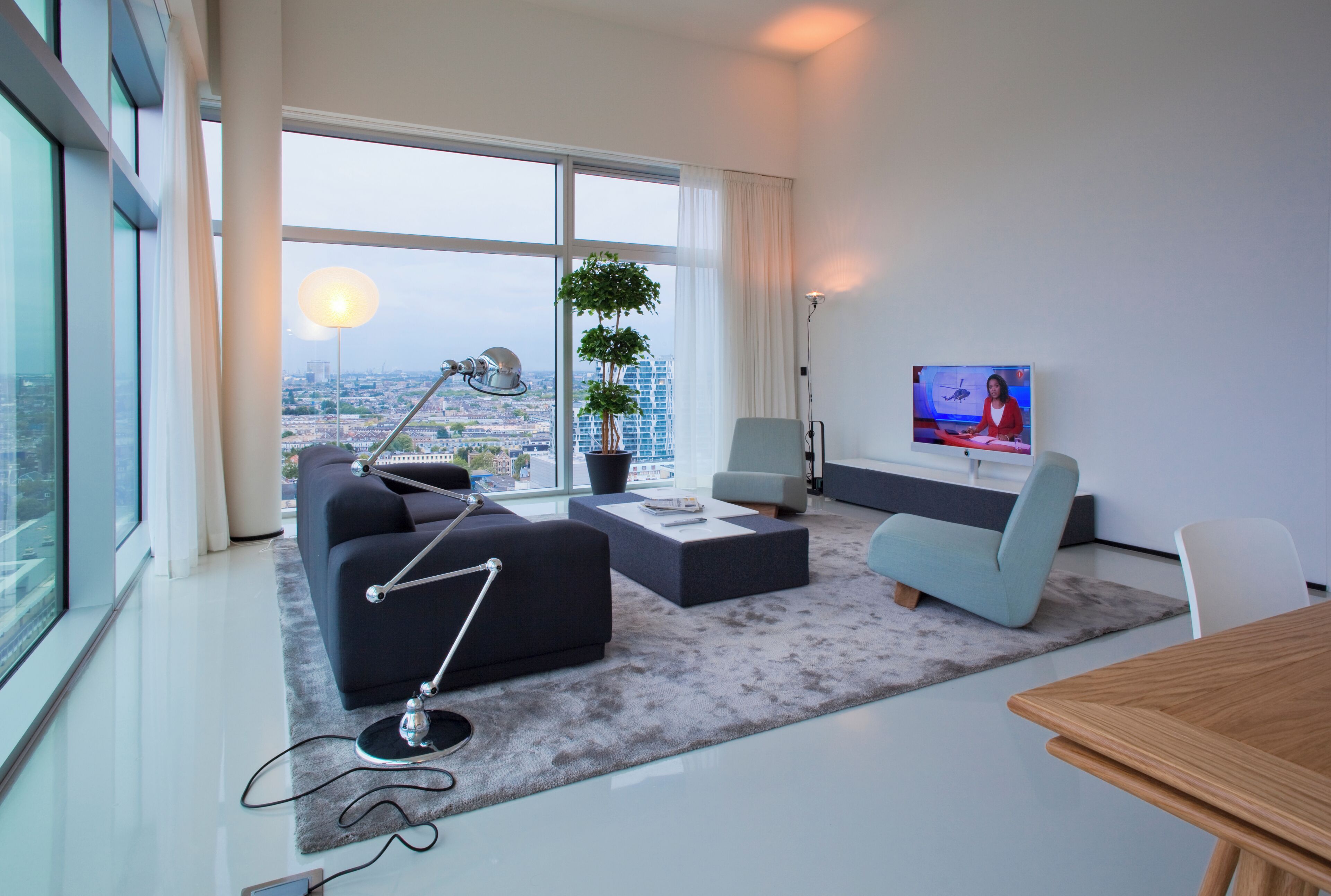 A modern living room with a large window, a sofa, a coffee table, a TV, and a dining table.