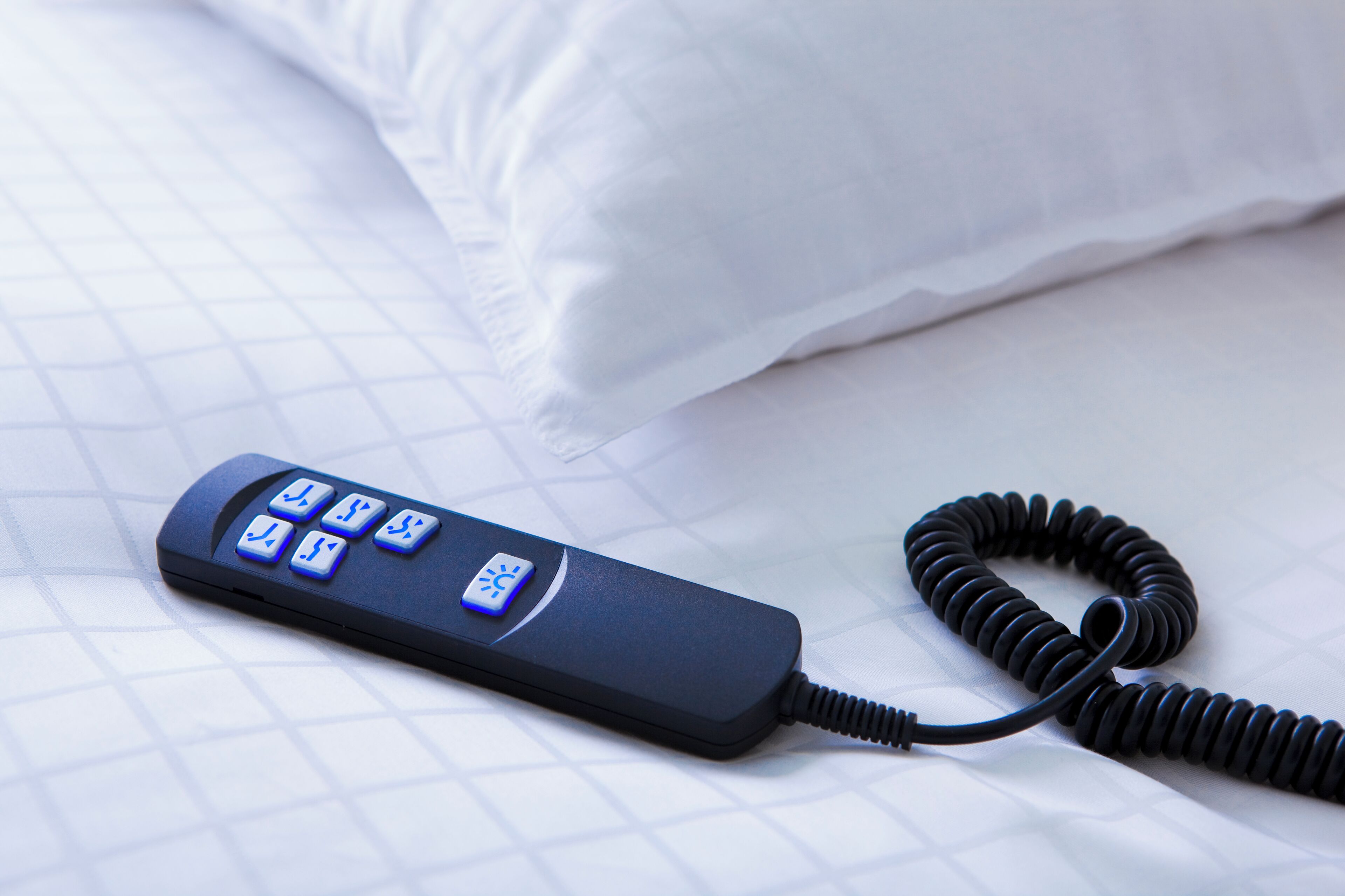 A black bedside phone with a coiled cord on a bed with a white pillow and a white pillowcase.