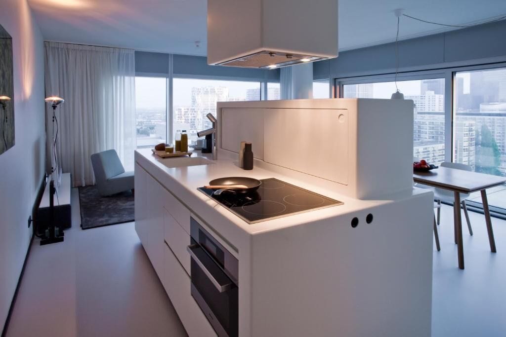 A modern kitchen with a built-in stove, a dining area with a table, and a view of the city through large windows.