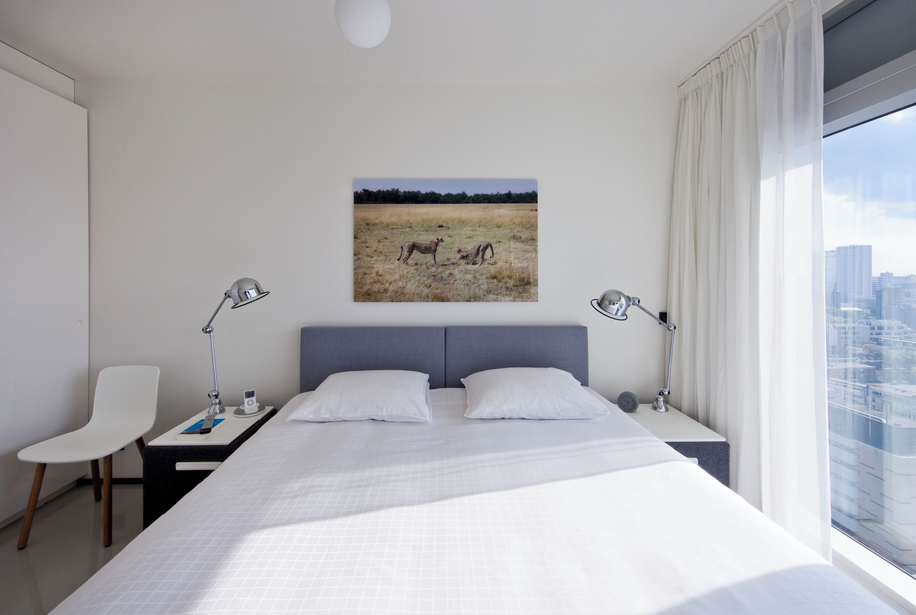 Une chambre d’hôtel moderne avec un grand lit, deux tables de chevet, un bureau, une chaise et une vue sur la ville par la fenêtre.