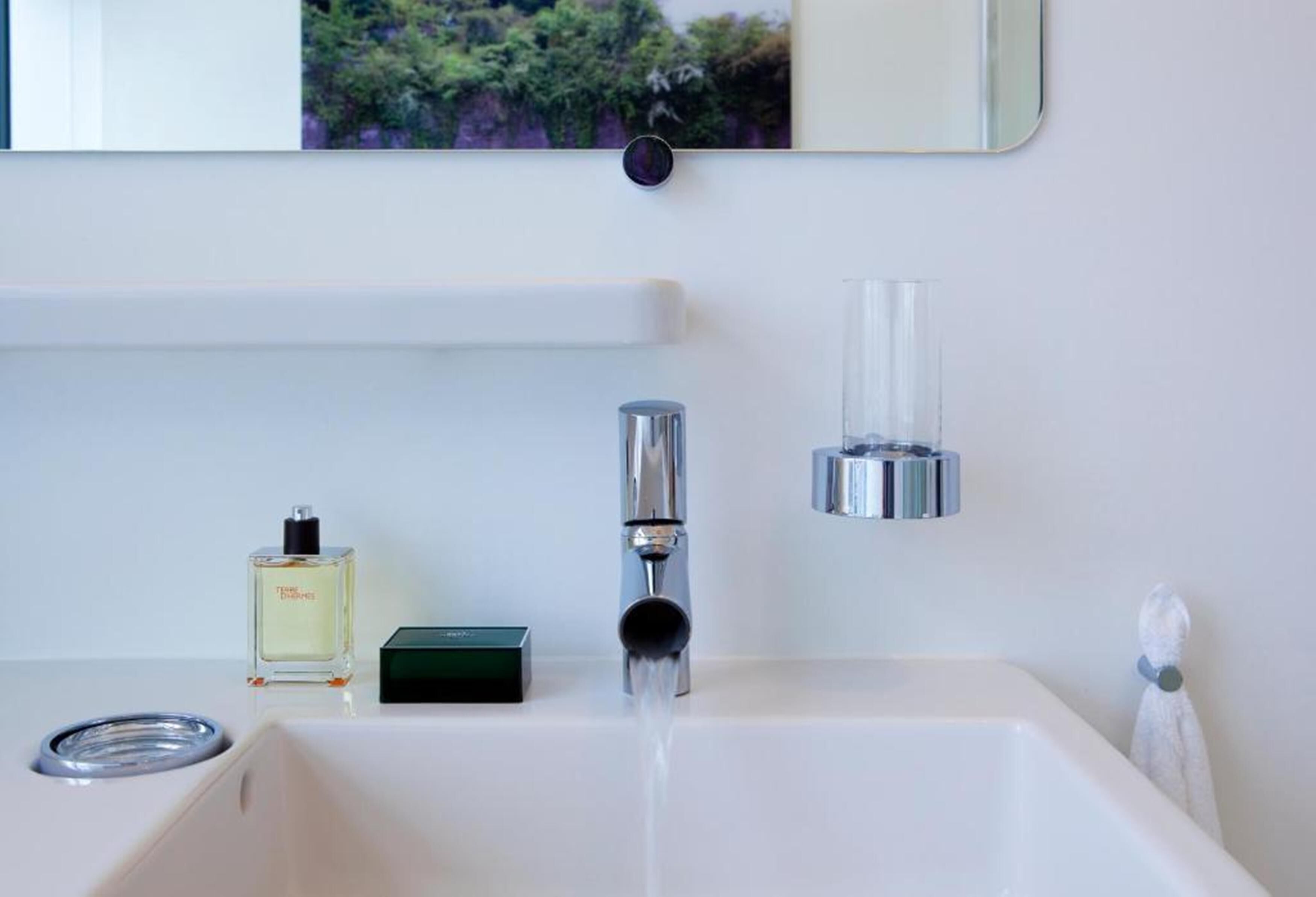 A modern bathroom with a white sink, a chrome faucet, a glass bottle of perfume, and a towel hanging on the wall.