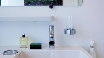 A modern bathroom with a white sink, a chrome faucet, a glass bottle of perfume, and a towel hanging on the wall.