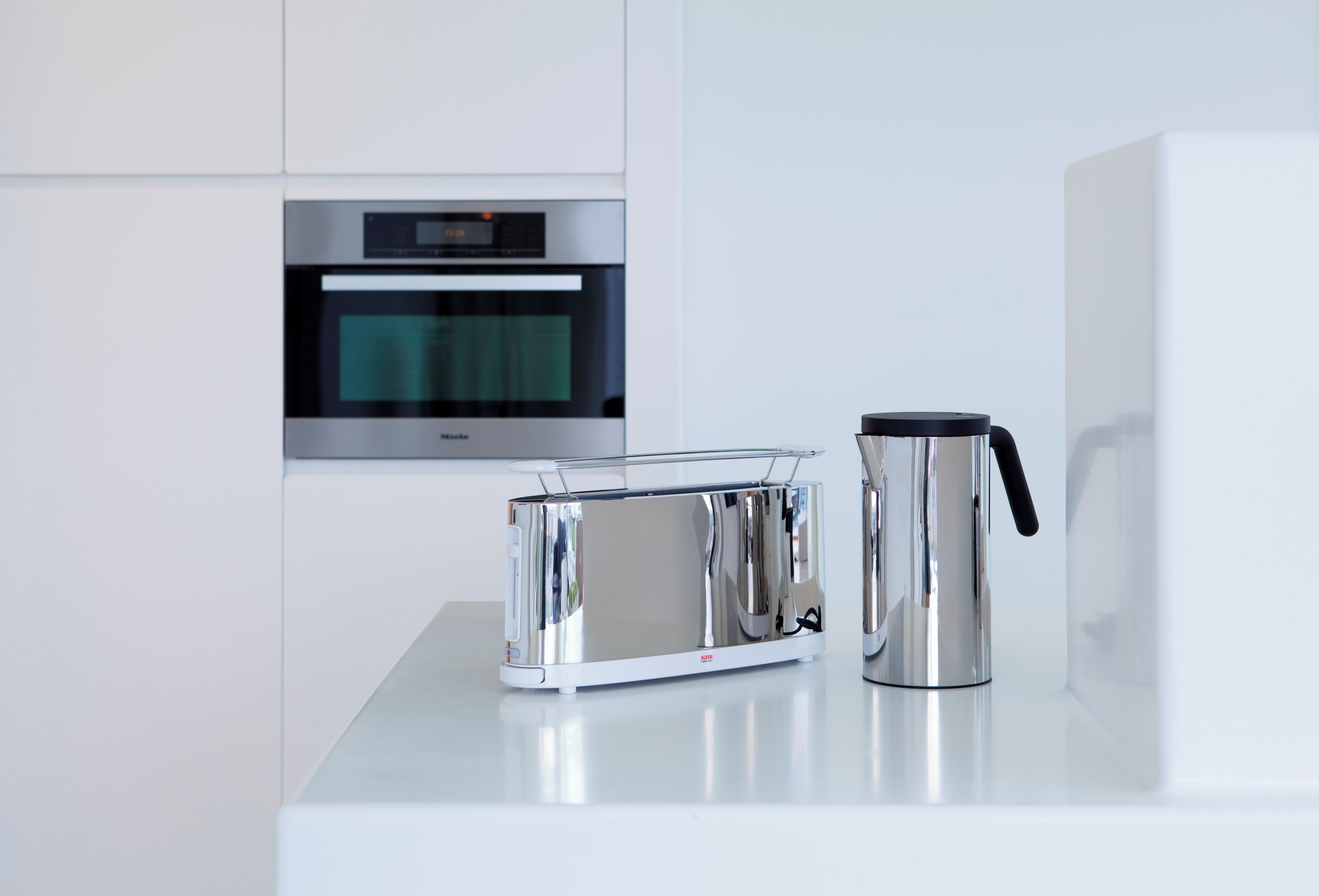 Eine moderne Küche mit einem Edelstahltoaster und einer Kaffeemaschine auf einer weißen Arbeitsplatte.