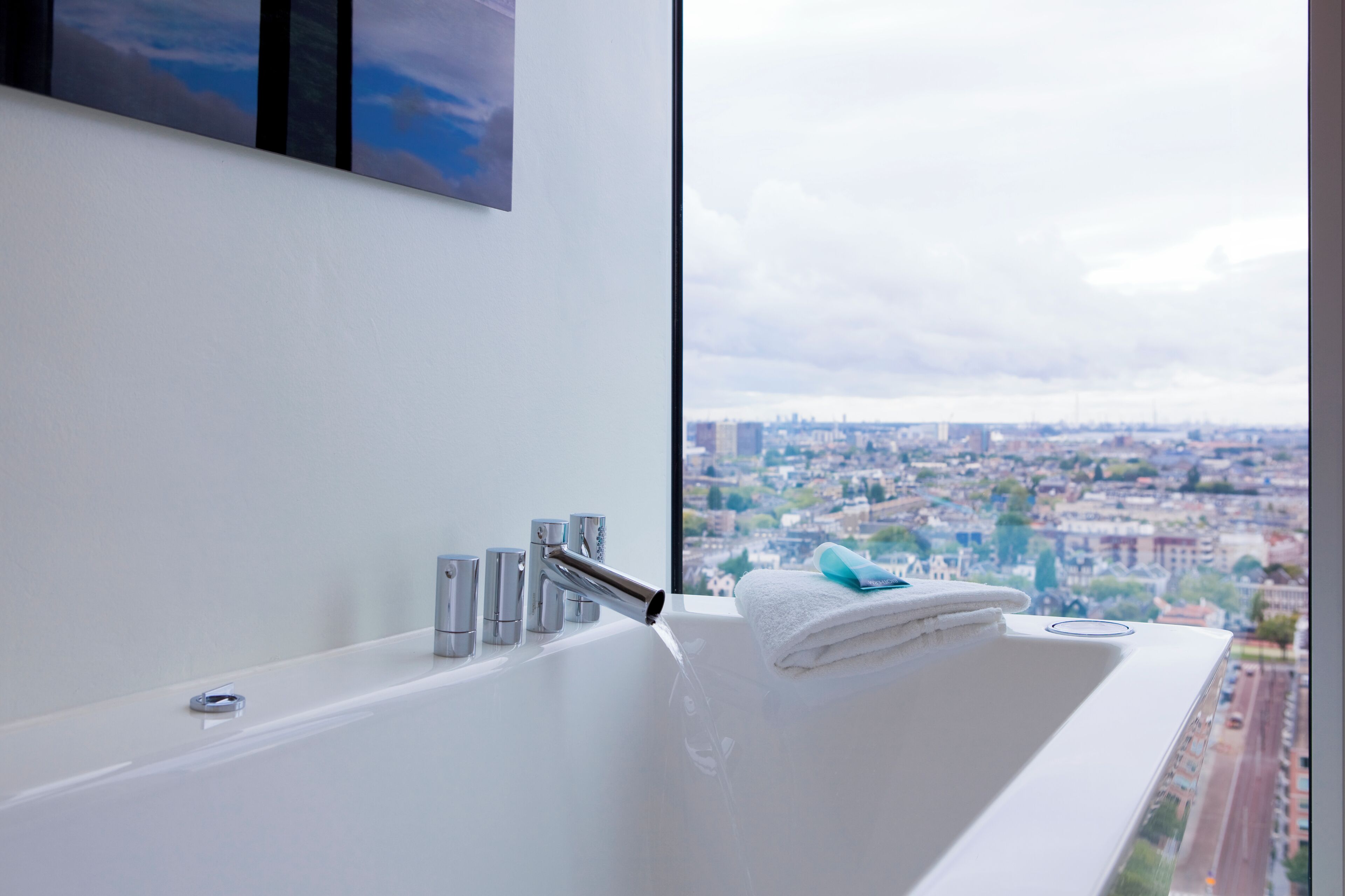 A modern bathroom with a bathtub, a window with a city view, and a towel on the edge.