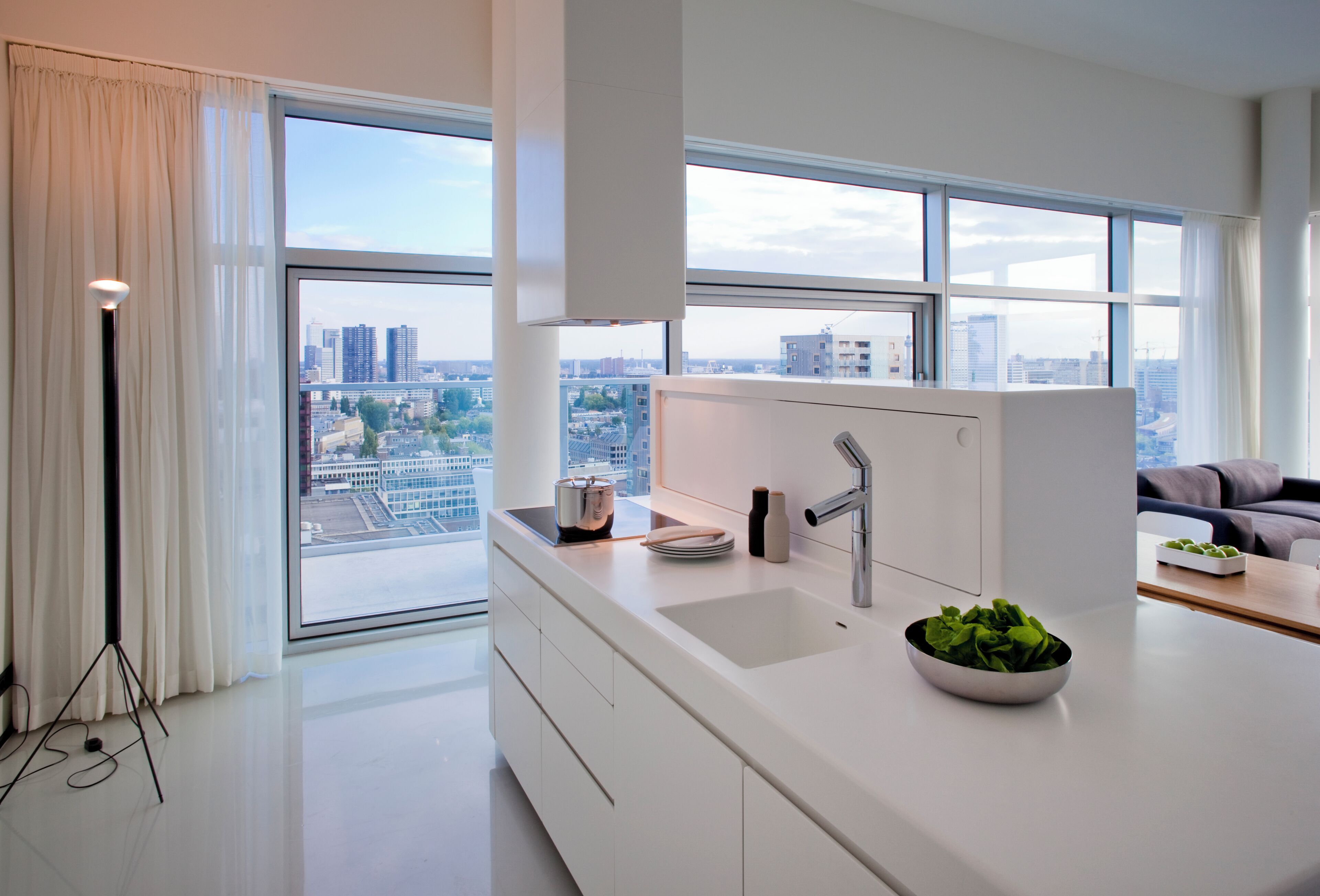 Eine moderne Küche mit einem großen Fenster, einer weißen Arbeitsplatte und einer Schüssel mit grünem Gemüse.