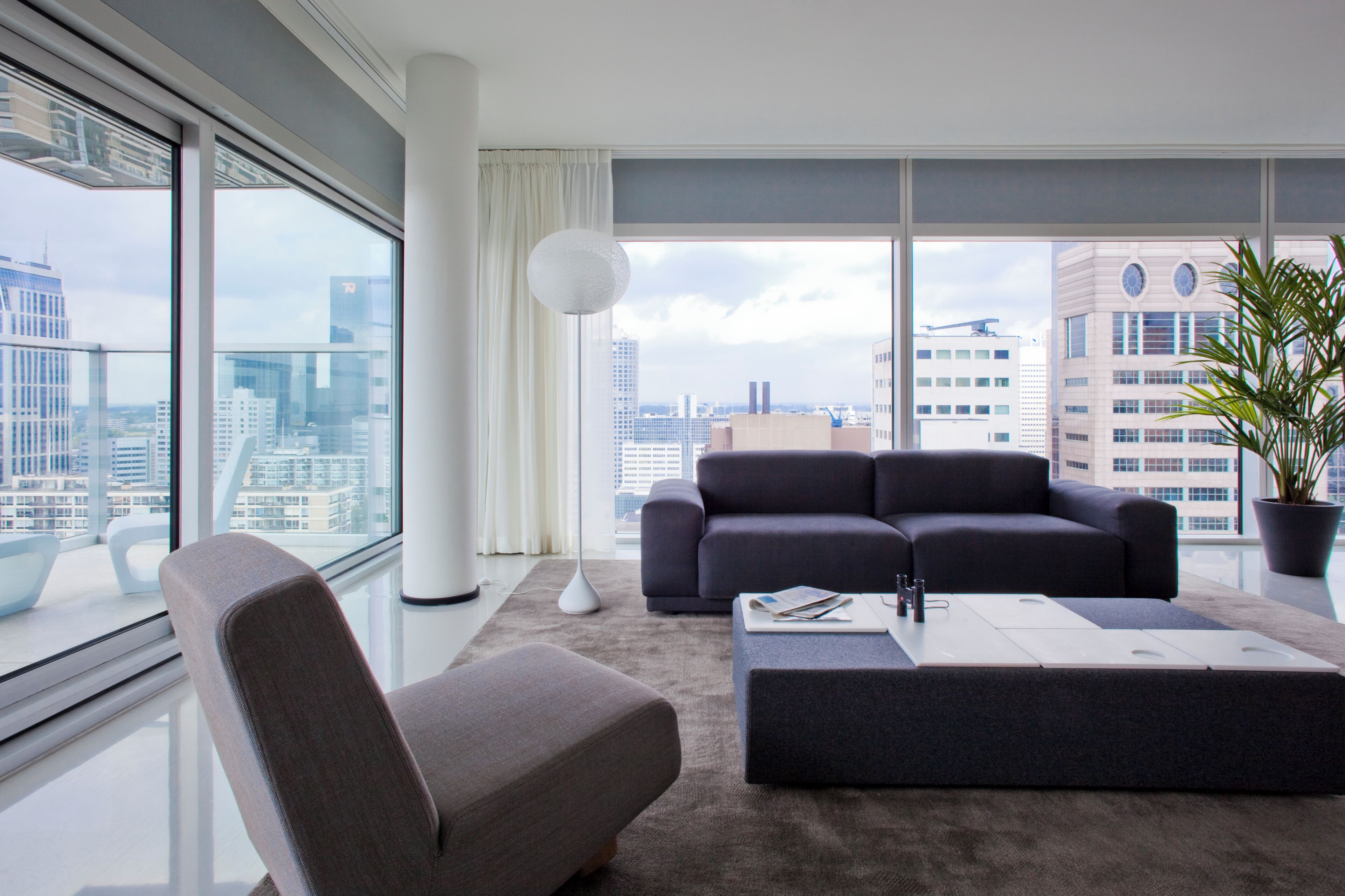 A modern living room with a grey sofa, a matching ottoman, and a large window offering a city view.