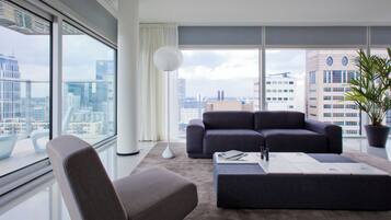 Ein modernes Wohnzimmer mit einem grauen Sofa, passendem Hocker und einem großen Fenster mit Blick auf die Stadt.