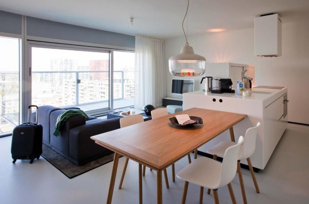 Een moderne hotelkamer met een zithoek, kitchenette en een groot raam met uitzicht over de stad.