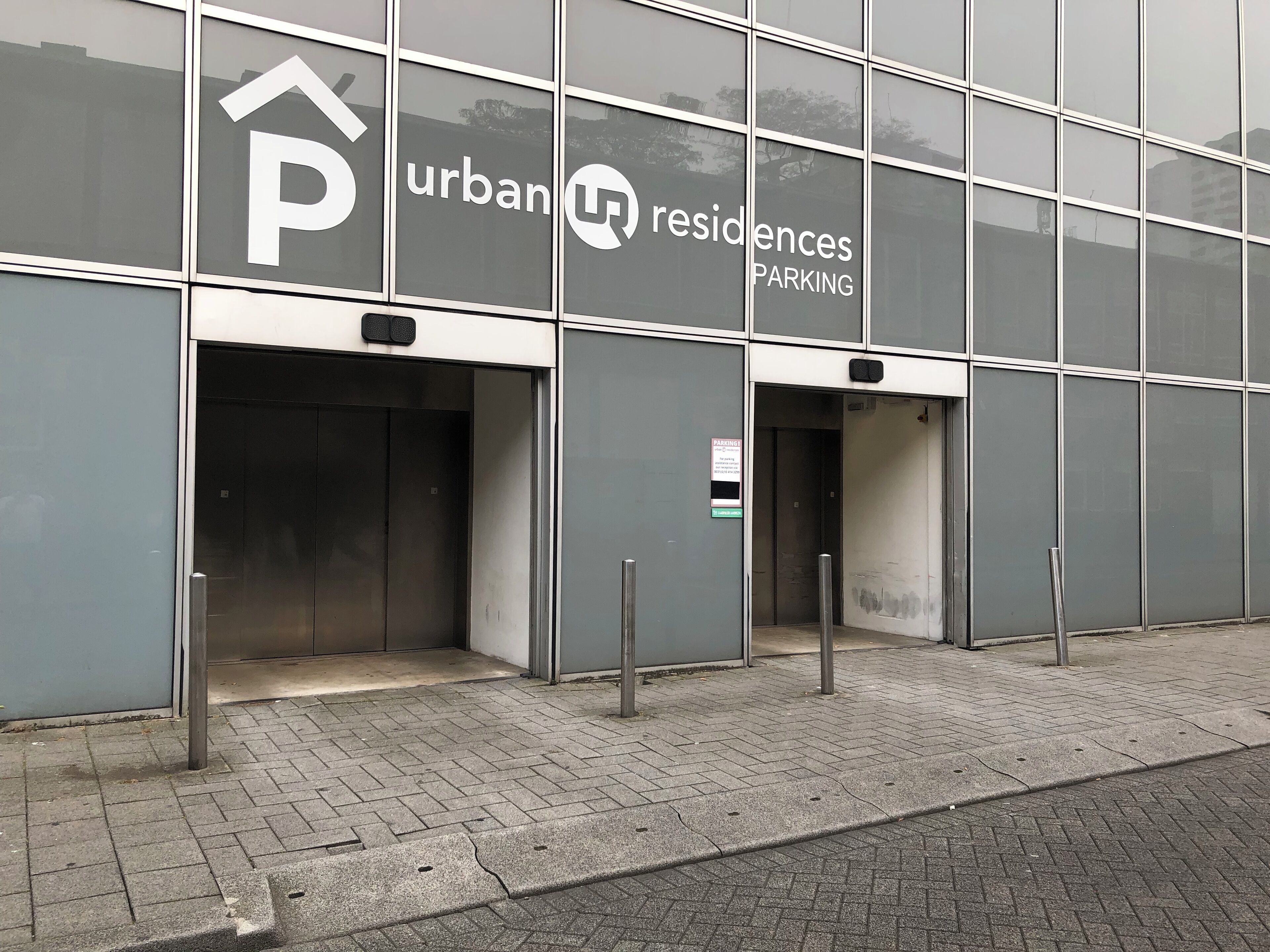 A modern building with a large glass facade, featuring a prominent 'Urban Residences' sign and a 'Parking' sign.