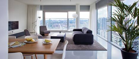 A modern living room with a dining area, large windows, and a city view.