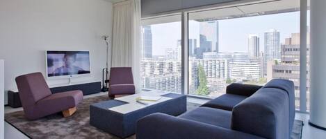 A modern living room with a large TV, comfortable seating, and a city view.