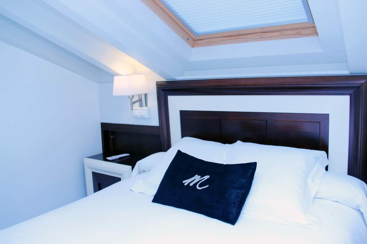 Een hotelkamer met een bed, nachtkastje, lamp en dakraam.