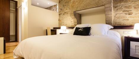 A bedroom with a large bed, wooden flooring, a stone wall, and a wooden door.