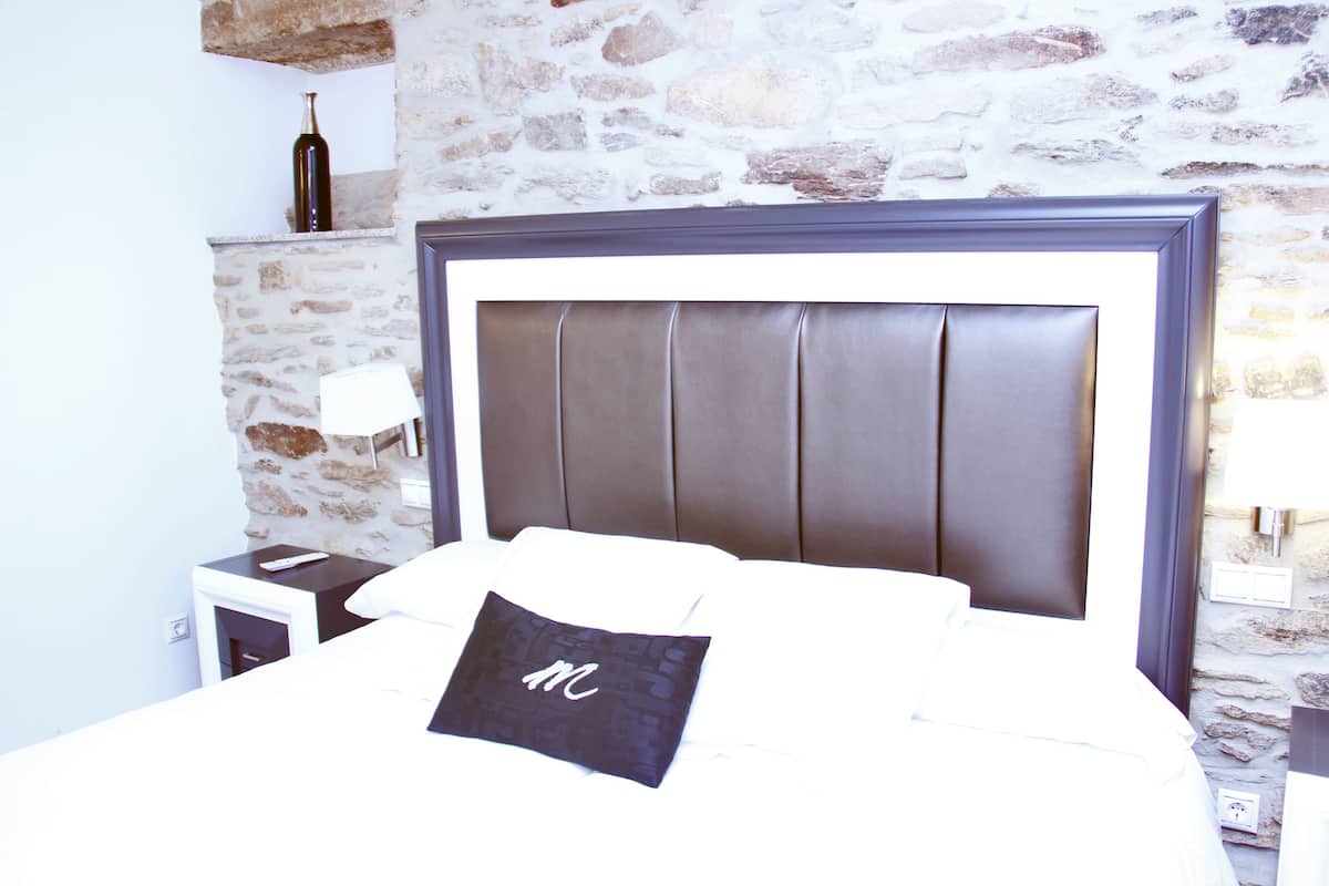 Een hotelkamer met een stenen muur, een bed met hoofdeinde, een nachtkastje, een lamp en een fles op de muur.