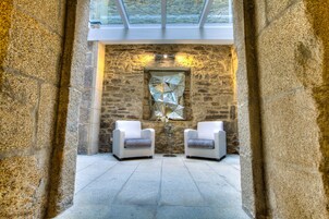 Una habitación con paredes de piedra, dos sillones blancos, una mesa de cristal y una obra de arte geométrica en la pared.