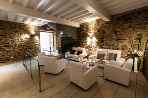 Una sala de estar moderna con paredes de piedra, muebles blancos y una escalera que sube a un nivel superior.