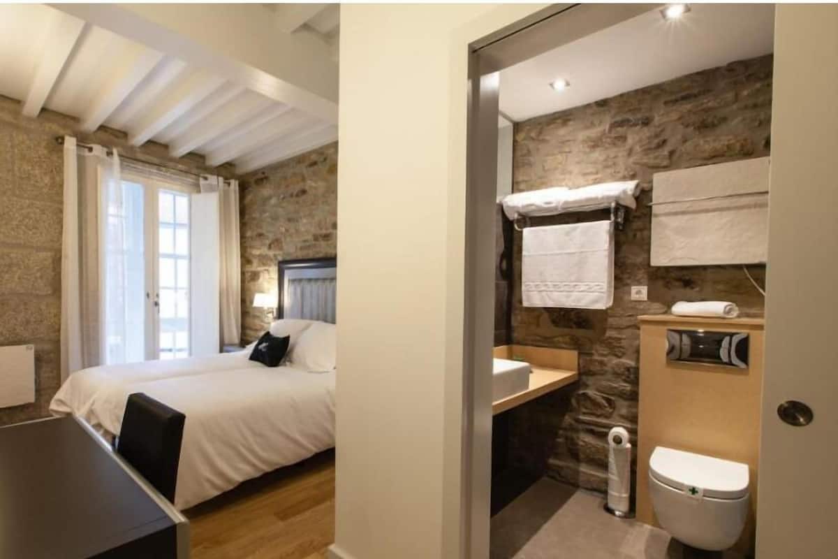 Een slaapkamer met een bed, een bureau en een badkamer met toilet en wastafel.