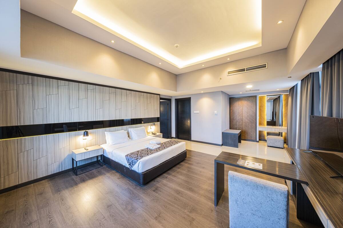 A modern hotel room with a large bed, bedside tables, a desk, and a mirror.