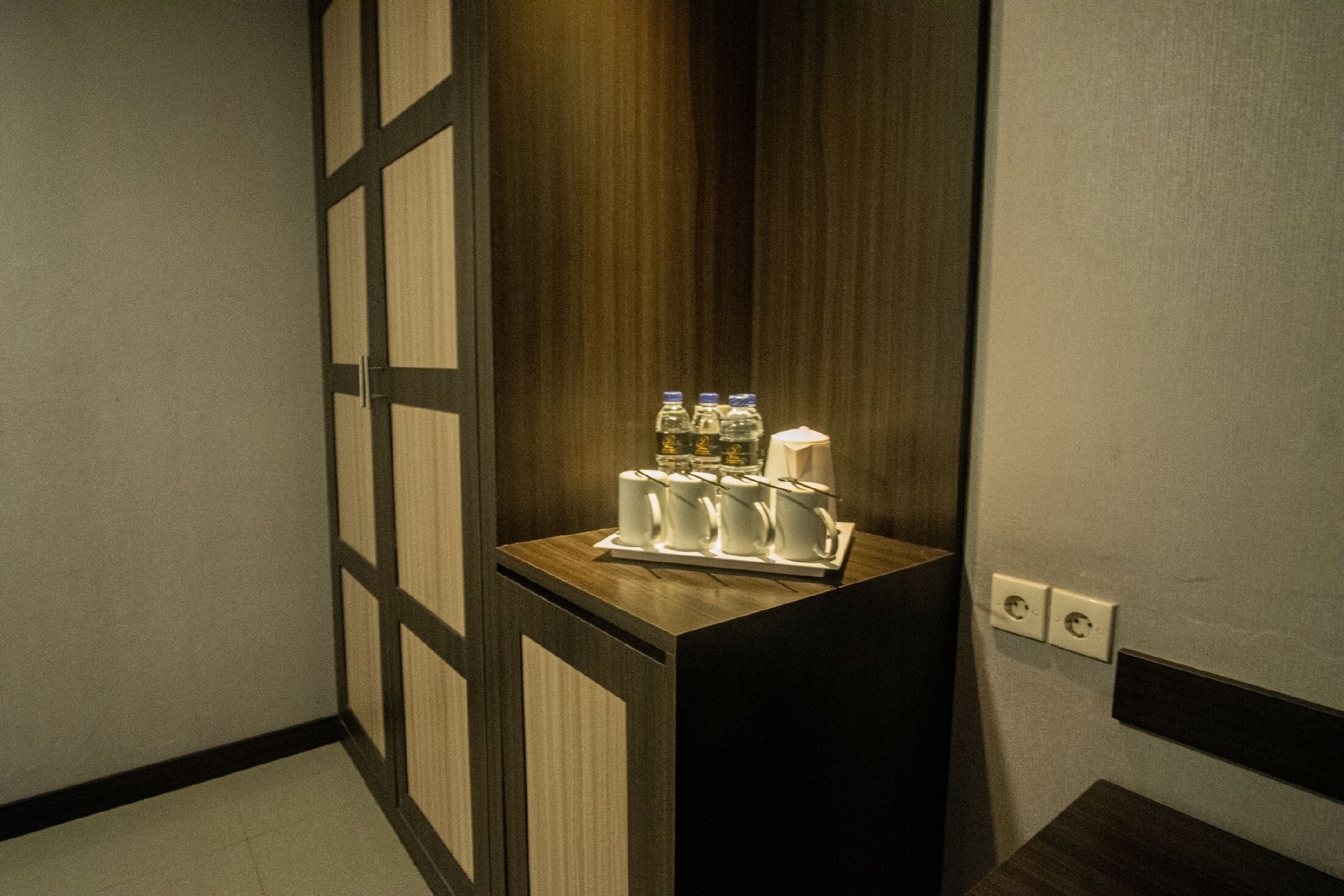 A small, dark wooden counter with a tray of white mugs and bottles.