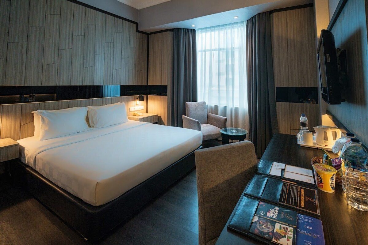 Une chambre d’hôtel avec un grand lit, un bureau avec une chaise, un téléviseur fixé au mur et une fenêtre avec des rideaux.